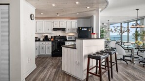 A modern kitchen with white cabinets, a black refrigerator, and a wooden ceiling.