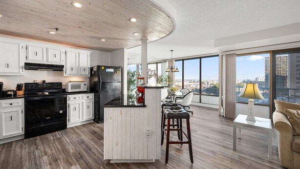 A modern kitchen with white cabinets, a black refrigerator, and a built-in island with bar stools.