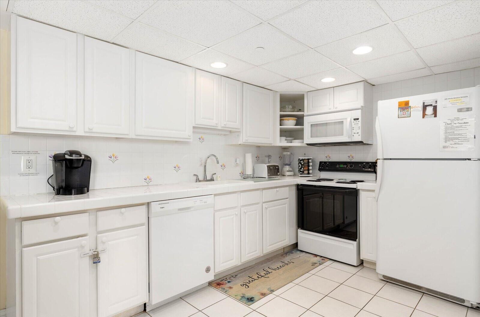 Una cocina moderna con armarios blancos, microondas, refrigerador y lavavajillas.