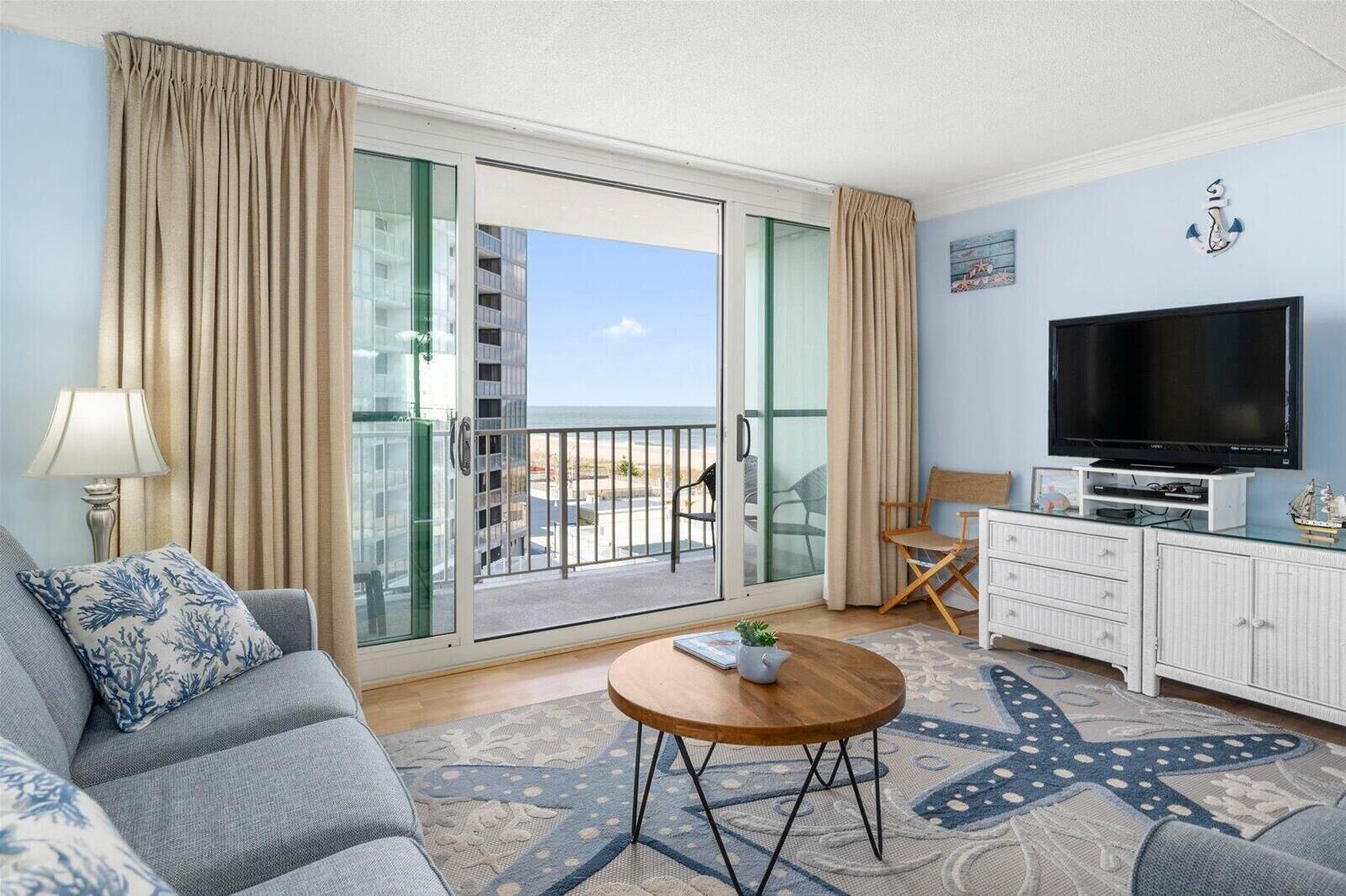 A hotel room with a balcony, a sofa, a television, and a small table.