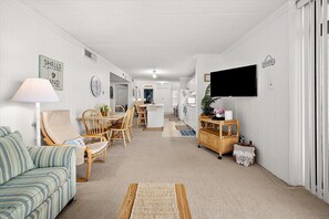 Un salon avec un canapé, une table à manger, des chaises, un téléviseur et, au fond, un coin cuisine.