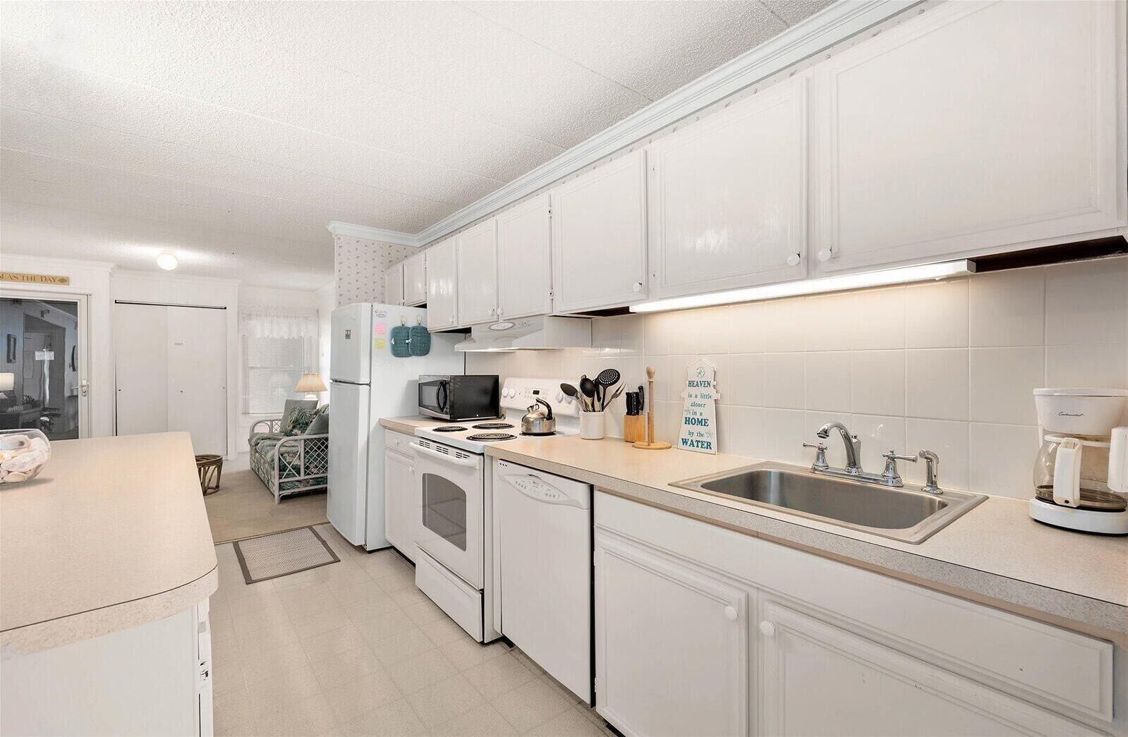 A modern kitchen with white cabinets, a stainless steel sink, a coffee maker, and a microwave.
