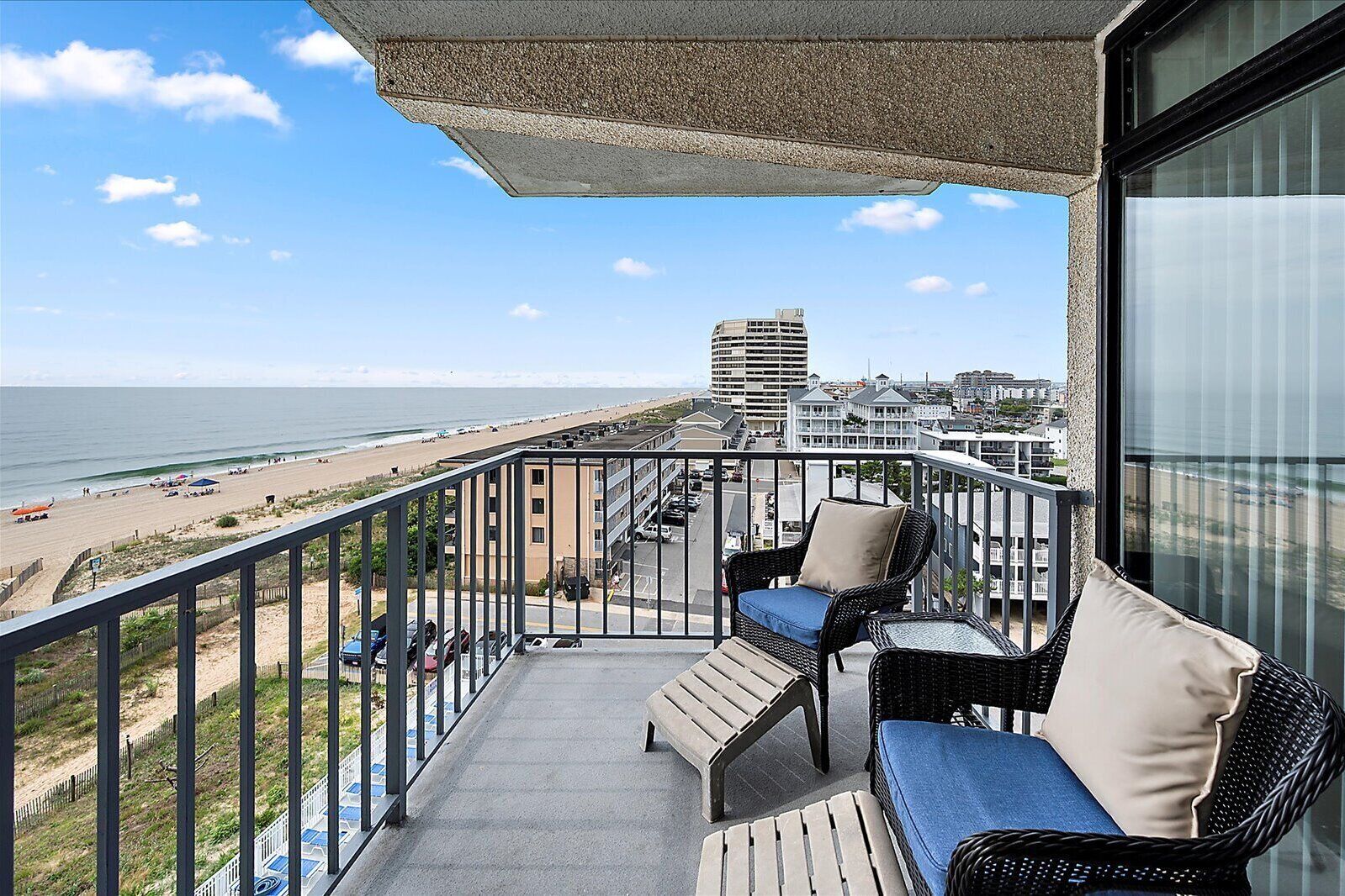 Ein Balkon mit Korbmöbeln, Blick auf den Strand und ein Parkplatz.