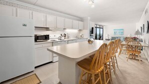 Une cuisine moderne avec des meubles blancs, un îlot central doté de chaises et un coin repas avec une table et des chaises.