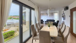Un comedor moderno con una mesa grande y sillas, vistas de la ciudad a través de amplias ventanas, y una sala de estar con sofás y una televisión.