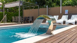 Una piscina con fuente acuática, rodeada de sillones de descanso y una pérgola.