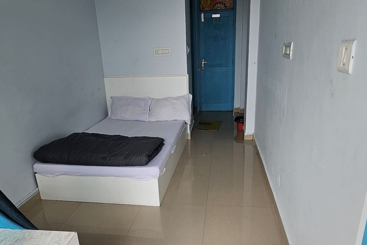 A room with a bed, a ceiling fan, a blue door, and a tiled floor.