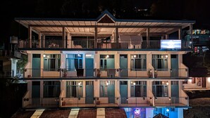 A multi-story hotel with balconies, a flat roof, and a neon sign. - LA SIESTA INDIA HOSTEL Mcleodganj (Dharamshala)