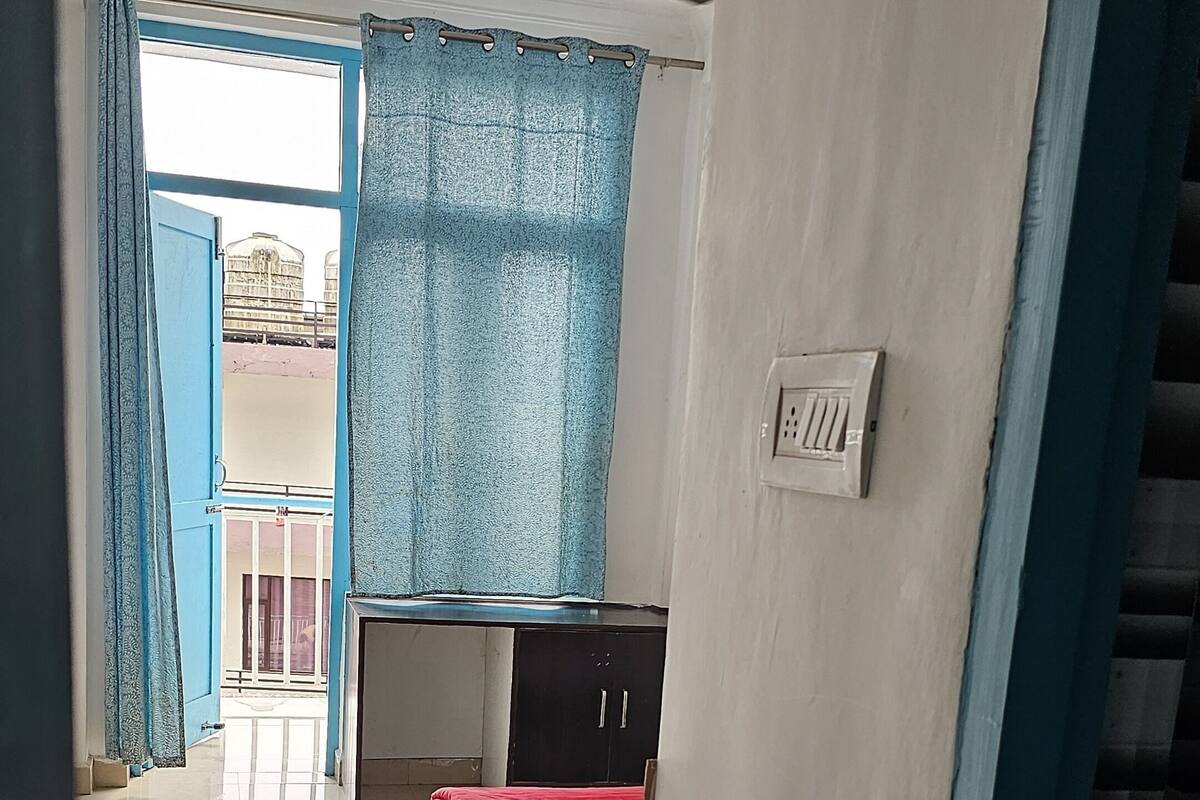 A bedroom with a bed, a wardrobe, a ceiling fan, and a view of the outside through a window with curtains.