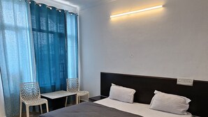 A modern bedroom with a large bed, a ceiling fan, a desk with chairs, and a patterned rug. - LA SIESTA INDIA HOSTEL Mcleodganj (Dharamshala)
