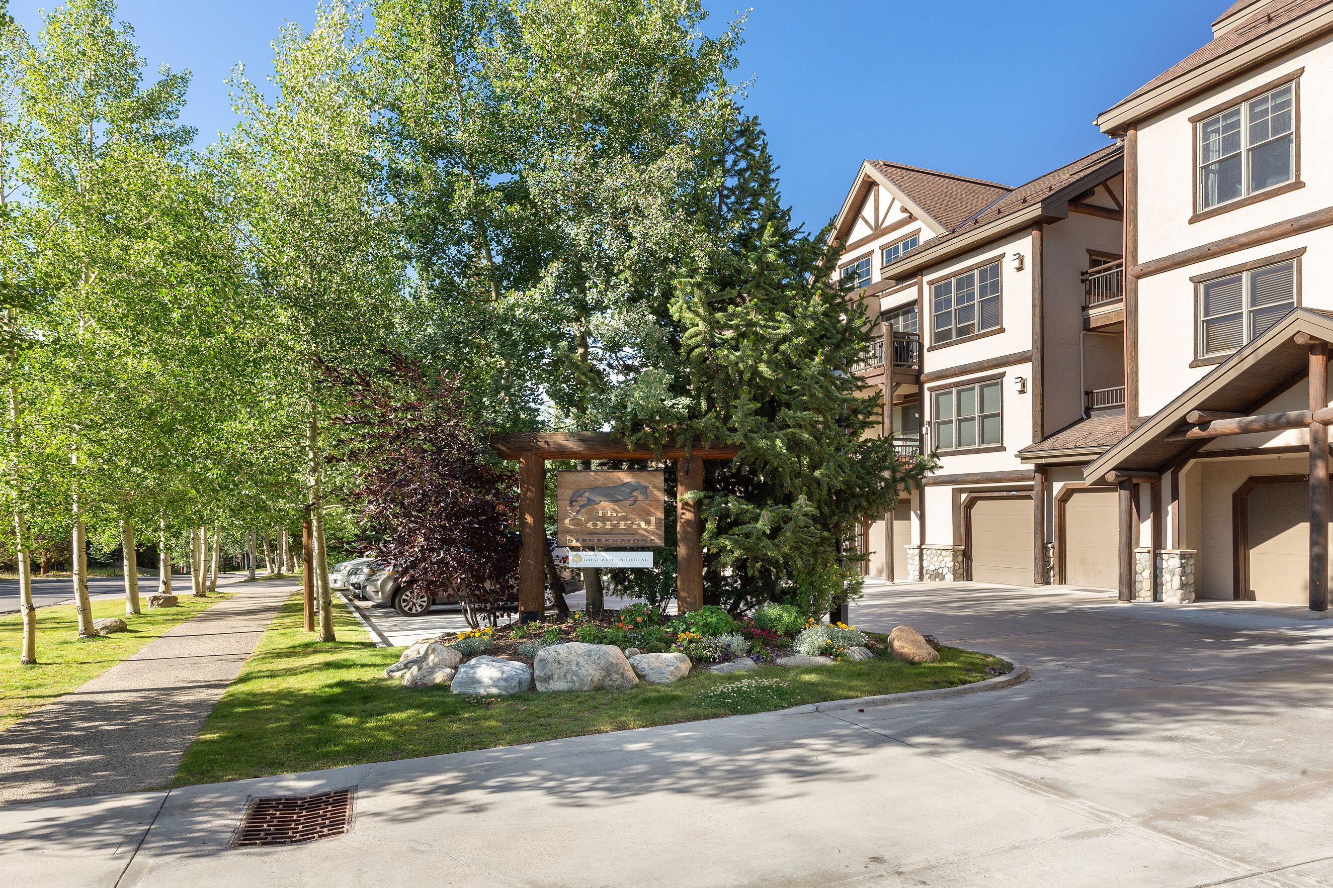 A residential area with a gated entrance, a signboard, and a driveway leading to a building with multiple garage doors.