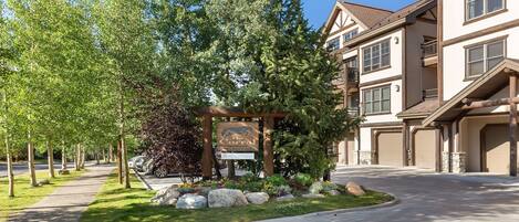 A residential area with a gated entrance, a signboard, and a driveway leading to a building with multiple garage doors.