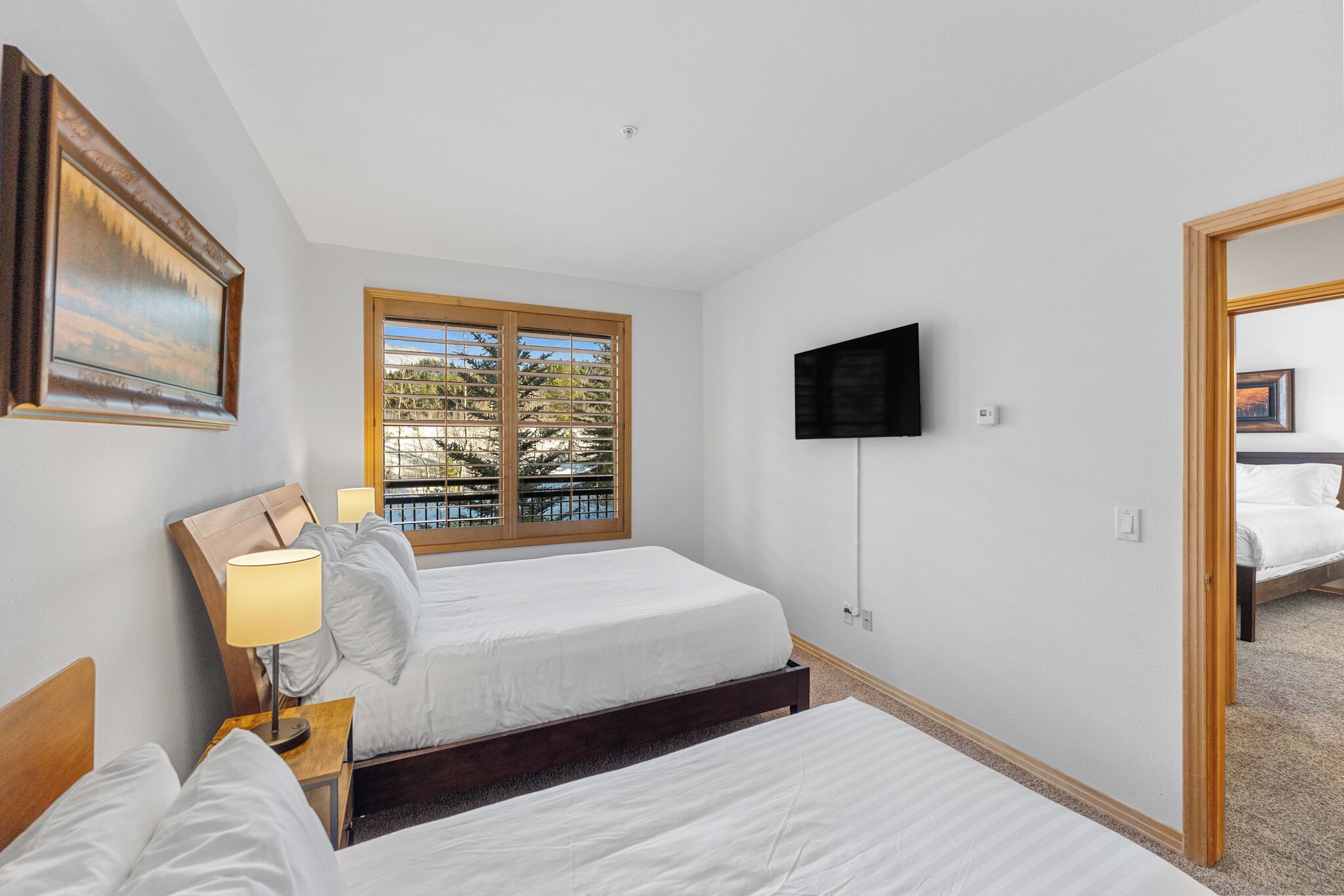 Een hotelkamer met twee bedden, een aan de muur bevestigde televisie en een raam met jaloezieën.