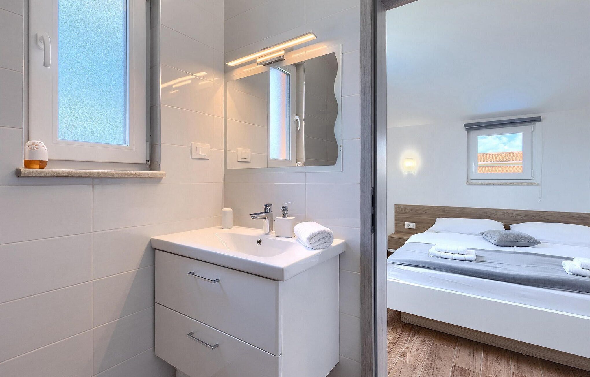 Een moderne badkamer met een wit wastafelmeubel, een spiegel en een raam.
