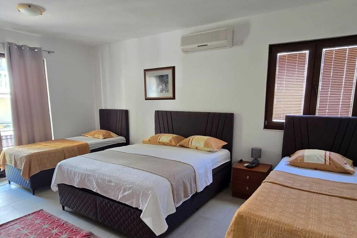 A hotel room with two beds, a red patterned rug, a framed picture on the wall, and a window with blinds.