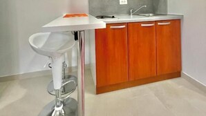A compact kitchen with wooden cabinets, a white countertop, and a stainless steel sink. - Apartments TP 777 (Budva)