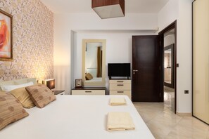 A bedroom with a bed, bedside tables, a TV, a mirror, and a door.