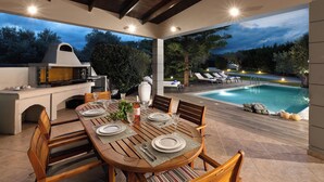 Un área de comedor al aire libre con piscina, barbacoa y sillones de descanso.