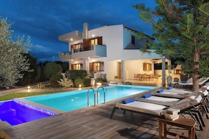 A modern two-story house with a swimming pool, lounge chairs, and a dining area.