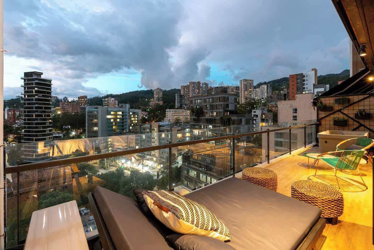 Un balcón con barandilla de cristal que da a una vista panorámica de la ciudad al anochecer.