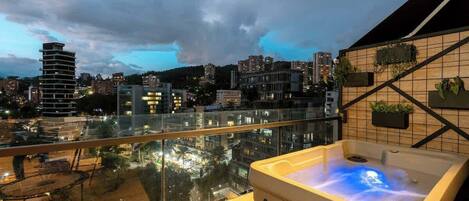 A balcony with a hot tub, city views, and a tiled wall with planters.