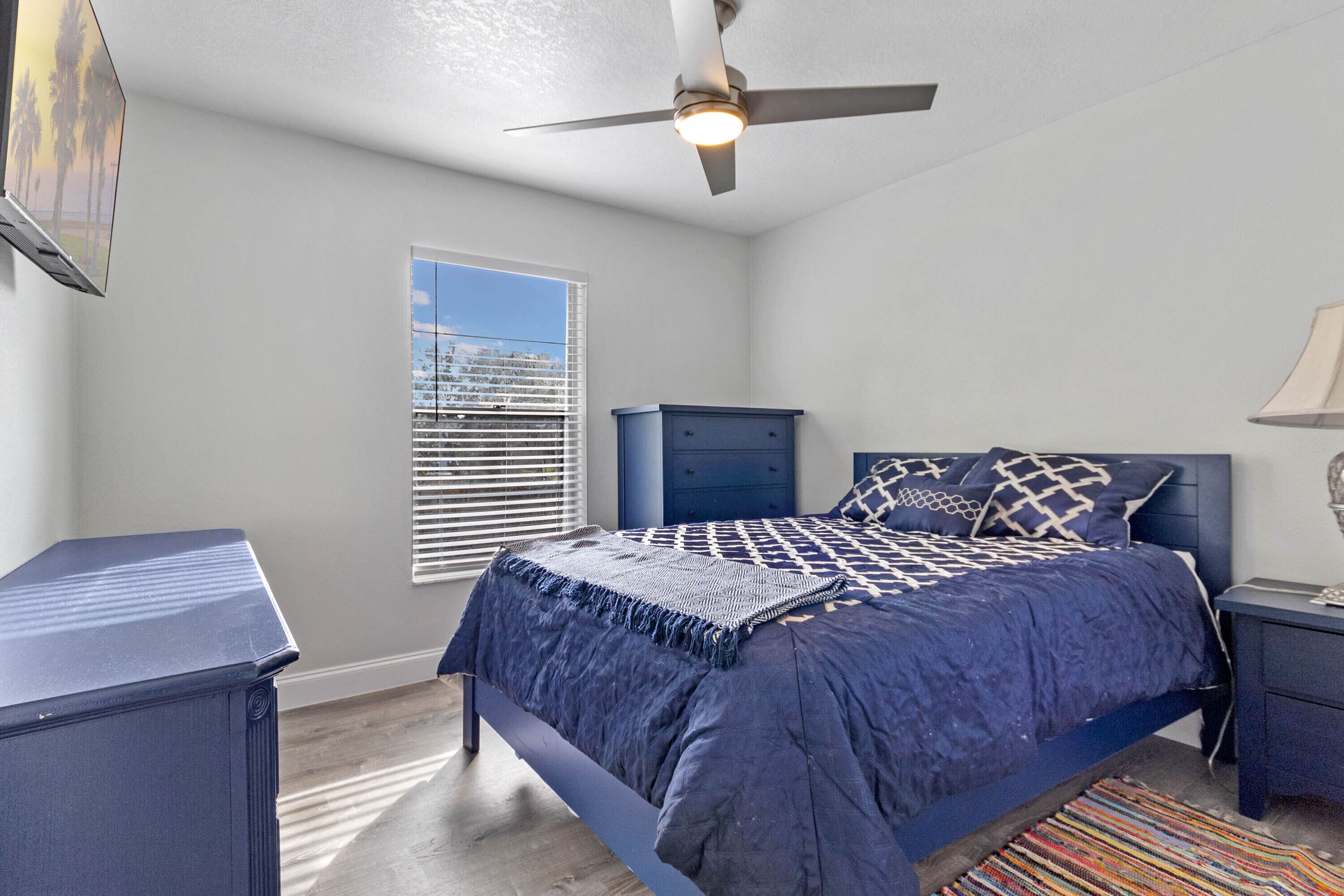 A bedroom with a bed, a ceiling fan, a nightstand, a dresser, and a window with blinds.