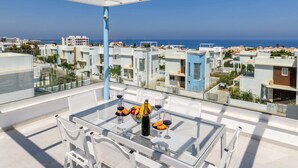 A rooftop terrace with a glass table, white chairs, and a bottle of wine. - Mylos Lifestyle Seaview Villa #21 (Paralimni)