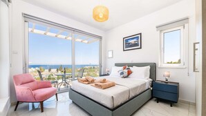 Ein Schlafzimmer mit Bett, Stuhl, Nachttisch und Meerblick.