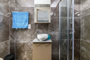 A modern bathroom with a glass shower enclosure, a white sink with a blue soap dispenser, and a blue towel hanging on a rack. - Mylos Lifestyle Seaview Villa #37 (Paralimni)