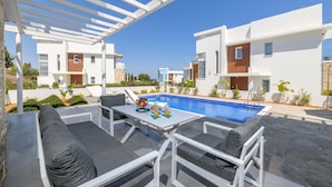 Ein moderner Poolbereich im Freien mit einer Pergola, Sitzgelegenheiten und blauem Himmel.