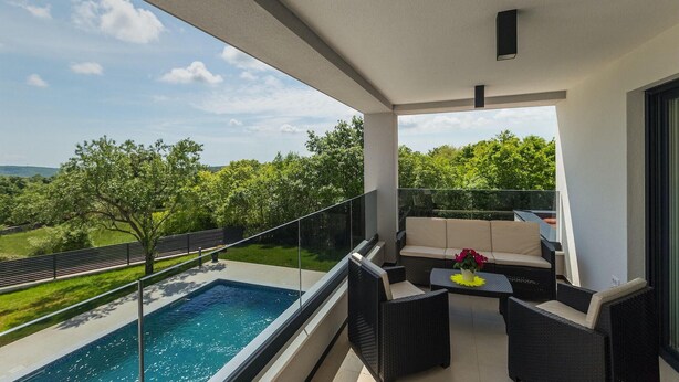A balcony with a pool, outdoor seating, and a view of greenery.