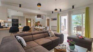 A modern living room with a brown sofa, a dining area, and a kitchen.