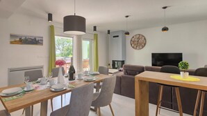 A modern living room with a sofa, a TV, and a dining area with a table set for two.
