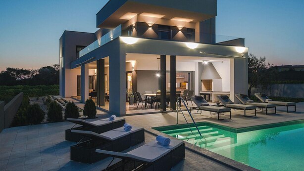 Una casa moderna de dos pisos amb piscina, seients a l'exterior i un porxo cobert.