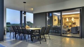 Zona de dinar moderna amb taula i cadires, lluminària penjant i vista de l'interior a través d'una porta de vidre.