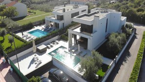 Una casa moderna de dos pisos amb piscina, zona d'estar a l'exterior i jardí.