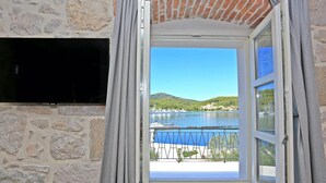 A room with a stone wall, a black TV mounted on it, and a window with curtains. - Beach front home in Preko (Preko)