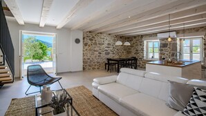 A spacious living area with a white sofa, a dining table, and a kitchen area with a stone wall. - Beach front home in Preko (Preko)
