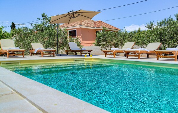 A pool with clear blue water, surrounded by wooden lounge chairs and a covered umbrella. - Beach front home in Preko (Preko)