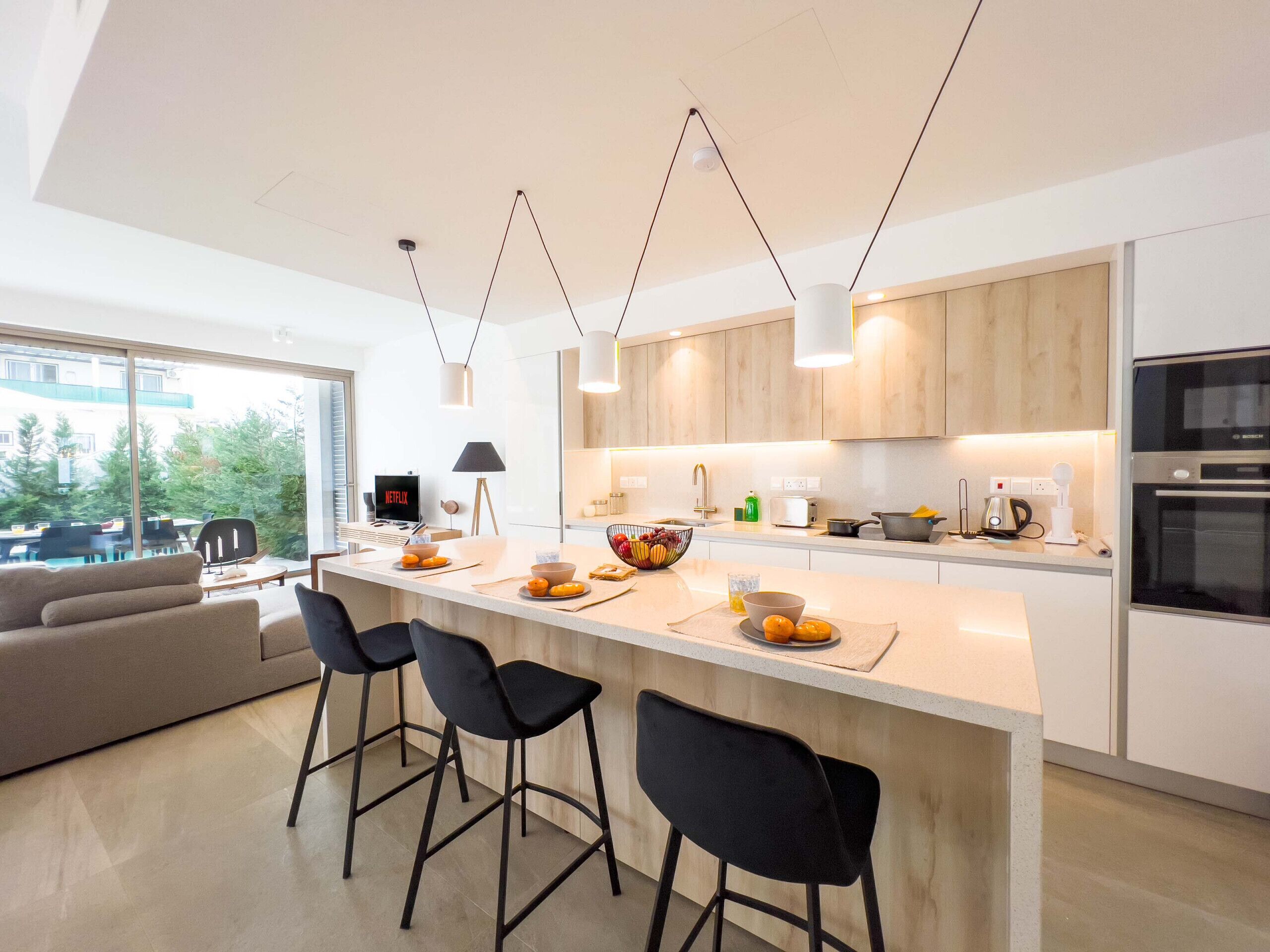 A modern kitchen with a central island, bar stools, and a dining area with a sofa.
