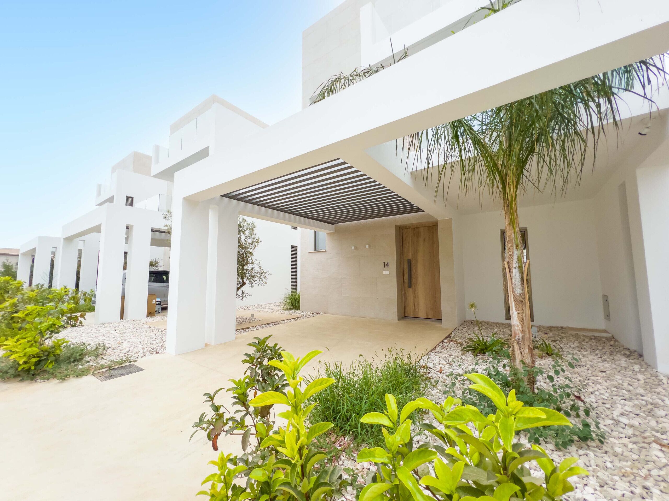 A modern building with a covered outdoor area, a door marked with the number 14, and surrounding greenery.