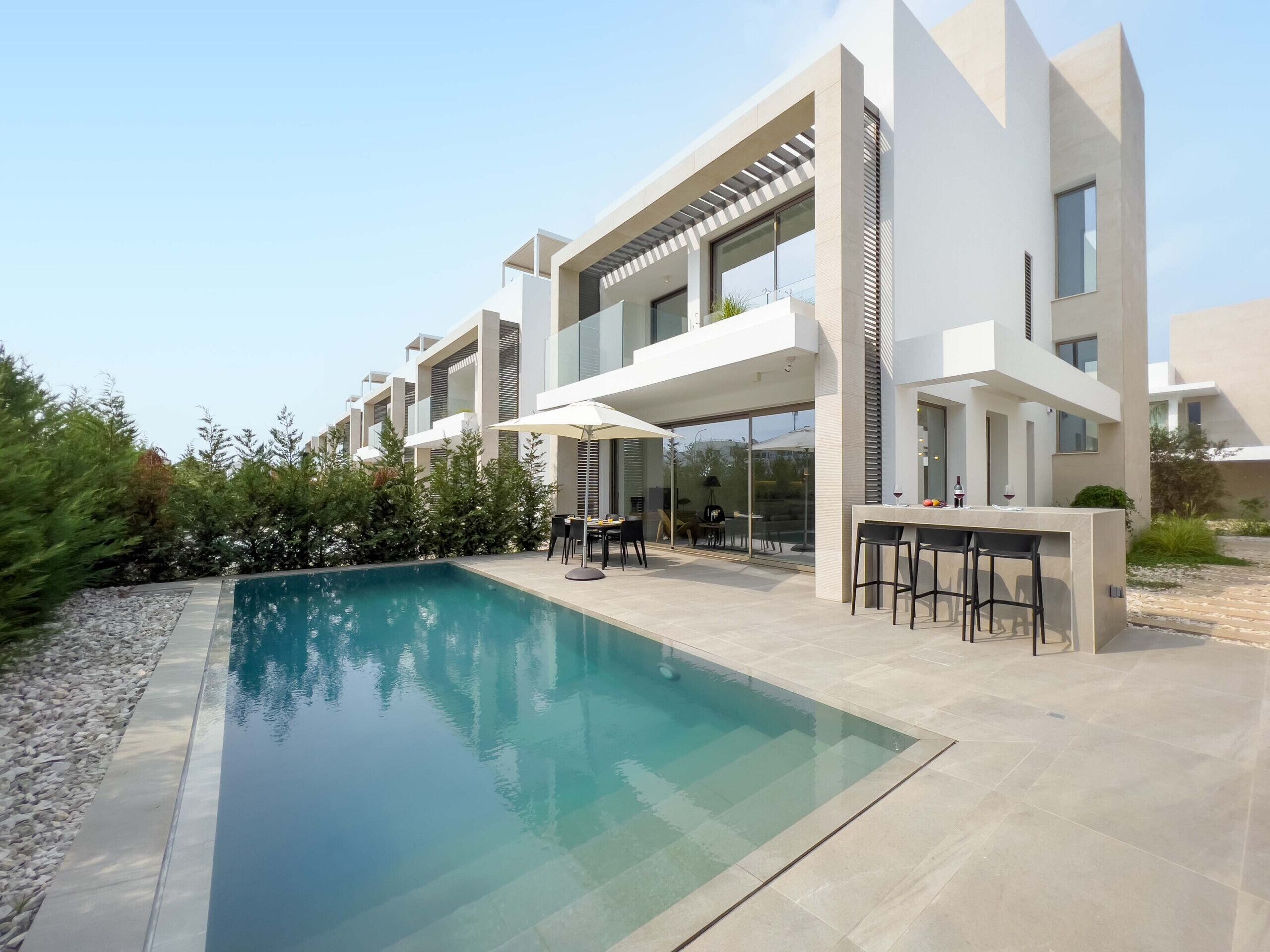 A modern residential building with a swimming pool, outdoor seating, and a patio area.