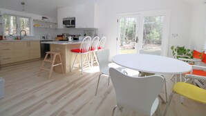 Une cuisine moderne avec des meubles blancs, un îlot central et un coin repas comprenant des chaises blanches et une table ronde.