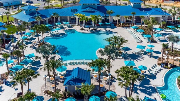 A resort with a large central pool, multiple lounge areas with umbrellas, and palm trees.
