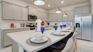 A modern kitchen with white cabinets, stainless steel appliances, and pendant lighting.