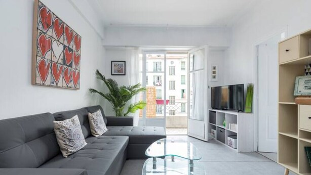 Un salon moderne avec un canapé gris, une table basse en verre et un téléviseur posé sur un meuble.