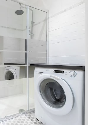 A modern bathroom with a glass shower enclosure, a built-in washing machine, and a tiled wall.