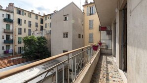 Un balcon étroit doté d’un sol carrelé, d’une rambarde en métal et offrant une vue sur les bâtiments voisins.