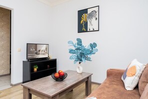 Uma sala de estar com televisão, uma mesa de centro com frutas, um sofá e uma obra de arte de zebra na parede.