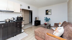 A modern kitchen with dark wood cabinets, a microwave, and a stove. There is a living area with a brown sofa and a small table with decorative items. - Stay Inn on Lusavorich 3 (Yerevan)